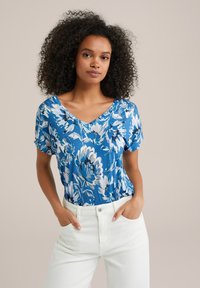 Zila ziedu raksta V-veida kakla tops ar īsām piedurknēm, izgatavots no viegla auduma. Iezīmē brīvu piegriezumu un kontrastējošas baltas bikses.