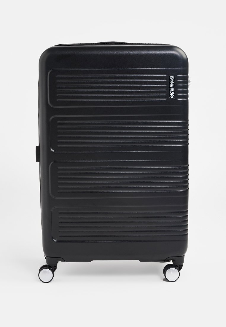 Black hard-shell suitcase with vertical ribbed texture, retractable handle, and four swivel wheels for easy mobility. Brand logo visible.