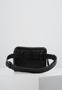 Czarna skórzana torba o teksturowanym wzorze, prostokątnym kształcie, regulowanym pasku i minimalistycznych elementach metalowych.