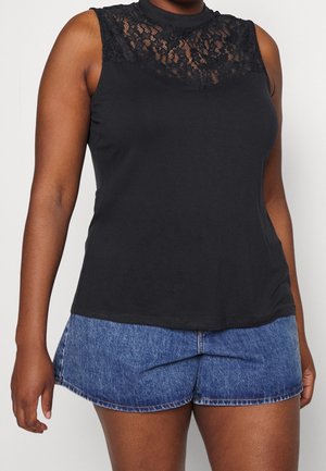 Haut noir sans manches avec empiècement en dentelle porté avec un short en denim bleu sur une personne devant un fond uni.