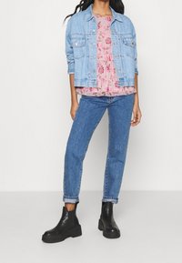 Světle modrá džínsová bunda, květinový růžový top s volány, klasické modré džíny a černé kotníkové boty s tlustou podrážkou.