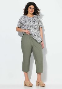 Korte mouwen, gepatternde top in grijs- en zwarttinten, gecombineerd met olijfgroene, cropped broeken en beige, geweven hakken.