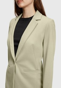 Blazer entallado verde claro con solapas muescas, cierre de un solo botón, dos bolsillos frontales, fabricado con una tela suave y elástica.