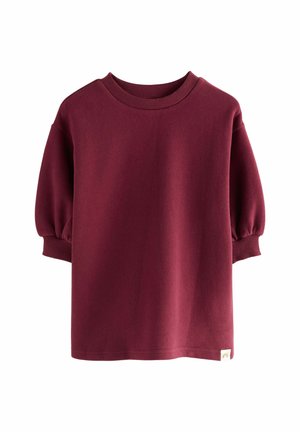 Felpa over-size bordeaux realizzata in tessuto morbido. Presenta un collo rotondo a costine e maniche corte a sbuffo. Include un piccolo tag con il logo.