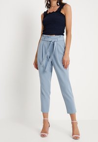 Námorně modrý crop top s nařasenými ramínky, spárovaný s světle modrými kalhotami s vysokým pasem a vázacími pásky na nohavicích. Růžové sandály.