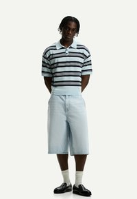 Polo a righe in azzurro chiaro e blu navy con due bottoni, abbinato a pantaloni shorts in denim azzurro chiaro e mocassini neri, completato con calze bianche.