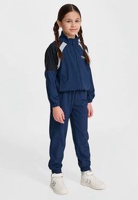 Mörkblå träningsdräkt i syntetmaterial med vita och svarta detaljer, med en jacka med dragkedja och matchande byxor med elastiska muddar.