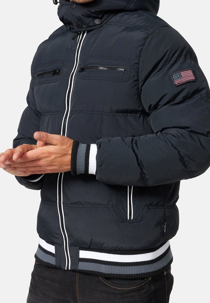 Laivaston sininen tikkitakki, jossa on irrotettava huppu, vetoketjut rinnataskuissa, resorit hihansuissa ja raidallinen vyötärönauha. Ominaisuuksiin kuuluu amerikkalaisen lipun kuvapatchi.