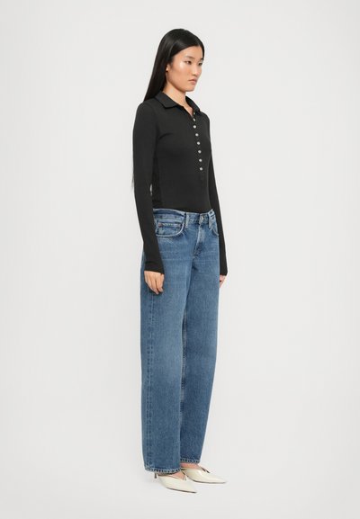 Black long-sleeve polo with button placket, paired with loose-fit blue jeans and white pointed-toe heels. Simple design, no visible patterns.