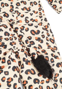Jumpsuit i leopardmönster i krämfärg med svarta och orange fläckar, med texturerade fickor och en svart pälsdelfinaccents för detaljer.