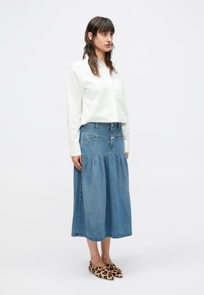 Λευκό πουκάμισο με κουμπιά, συνδυασμένο με μπλε τζιν φούστα μάξι με σούρες στο κάτω μέρος και τσέπες, ολοκληρωμένο με παπούτσια με λεοπάρ σχέδιο.