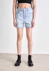 Světlé modré džínové šortky s vysokým pasem, pěti kapsami a ohrnutými lemy, spojené s černými šněrovacími kotníkovými botami.