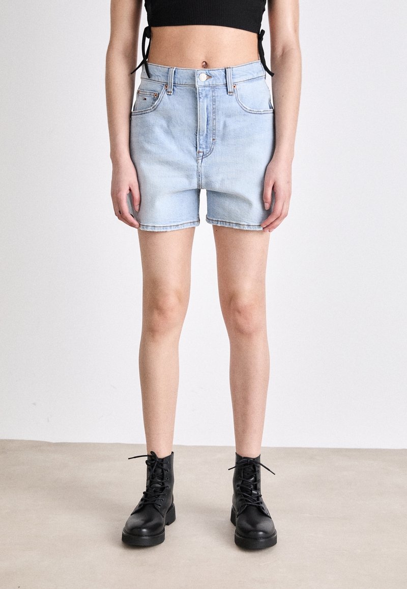 Světlé modré džínové šortky s vysokým pasem, pěti kapsami a ohrnutými lemy, spojené s černými šněrovacími kotníkovými botami.
