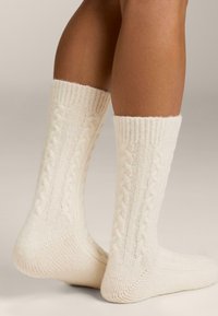 Kremne nogavice iz pletenega kabla z rebrastim robom, z mehko teksturo in strukturo. Opozarjajo na detajle na strani, ki izboljšajo vizualno privlačnost.