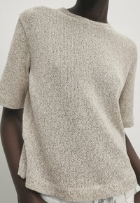 Beige neulepusero lyhyillä hihoilla, rento istuvuus ja pyöreä pääntie, jossa on teksturoidun kankaan ja sivuhalkion helmassa.