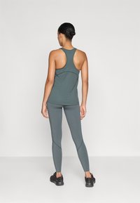 Sötétzöld, ujjatlan, racerback kialakítású top, passzoló, testhezálló leggings-gel párosítva. Mindkettő sima, nyújtható anyagból készült.