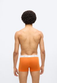 Πορτοκαλί βαμβακερά μποξεράκια με λευκή ζώνη μέσης που φέρει το λογότυπο "Tommy Hilfiger". Πλάγια όψη του ενδύματος που εμφανίζεται σε μοντέλο.