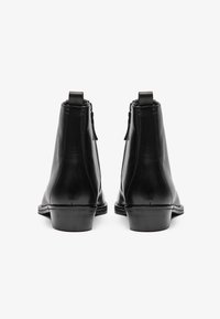 Botas de tobillo de cuero negro con un acabado liso, cierre de cremallera y tacón pequeño. Presenta costuras reforzadas y lengüetas en la parte posterior.