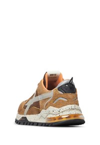 Zapatilla con una mezcla de gamuza color tostado y marrón, una suela blanca moteada, acentos naranjas y una pestaña negra en el talón con detalles del logo.