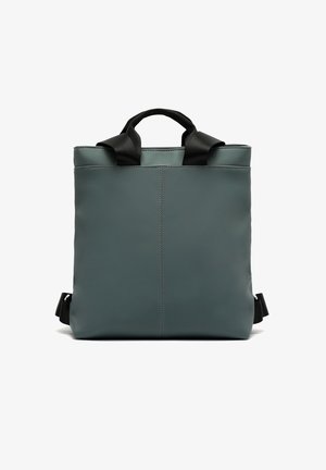 Sac à dos de forme carrée, vert foncé avec anses et bretelles noires, design simple, couture verticale centrée, présenté sur fond blanc.