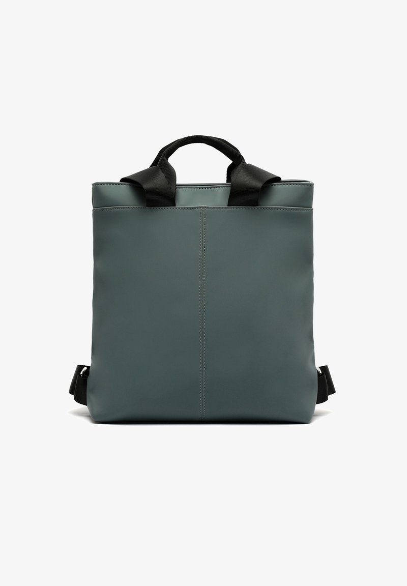 Sac à dos de forme carrée, vert foncé avec anses et bretelles noires, design simple, couture verticale centrée, présenté sur fond blanc.