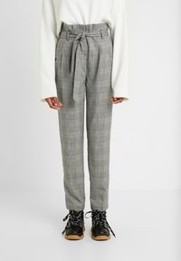 Gray plaid trousers with a high waist, a belt tie, and side pockets. Paired with black lace-up boots featuring a rubber sole.