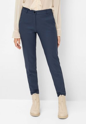 Marineblauwe slim-fit broek met een soepele textuur, voorzien van een knoopsluiting en riemlussen, gecombineerd met een crèmekleurige top van stof en beige ritslaarzen.