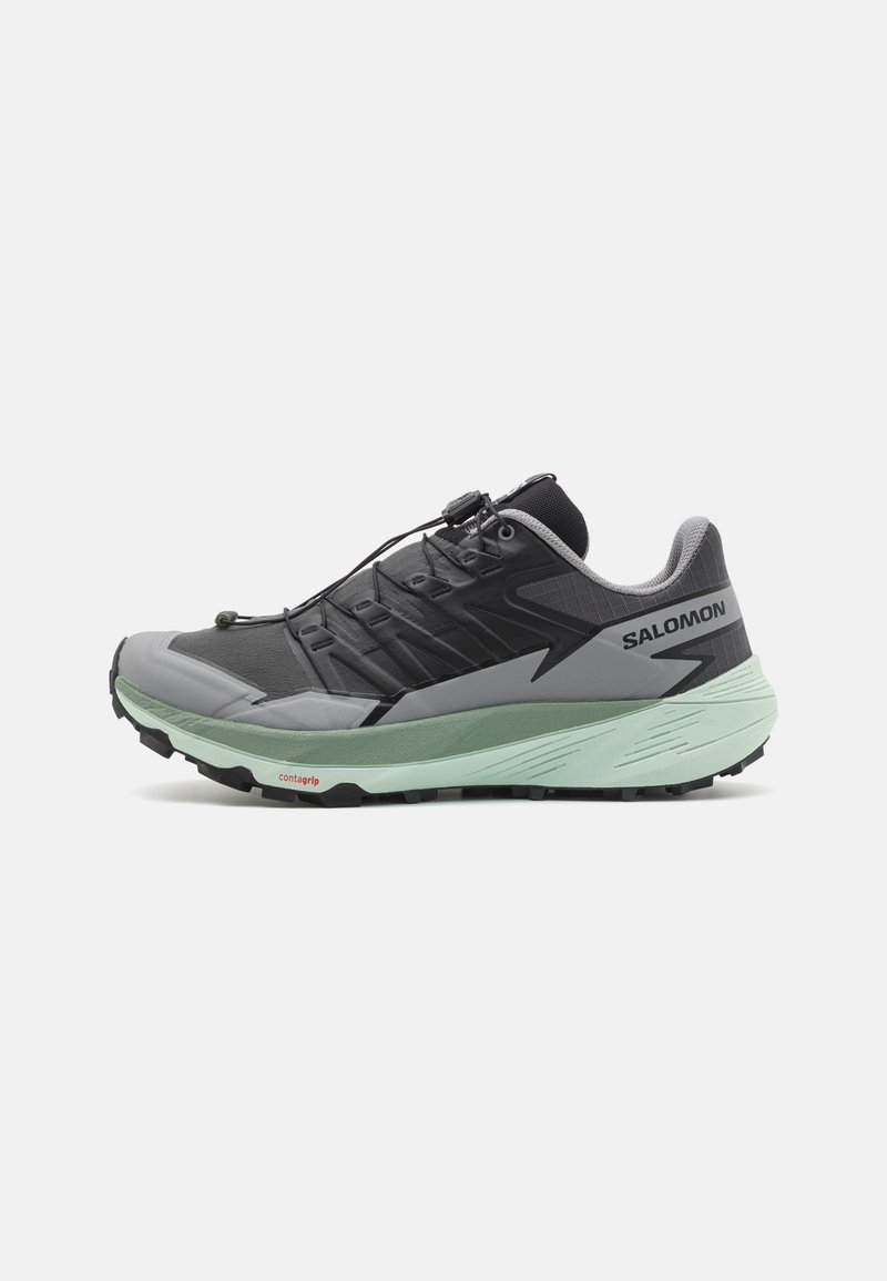 Zapatilla deportiva negra y gris con una entresuela verde menta, parte superior texturizada, sistema de lazado y suela robusta para tracción.