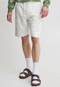 Lysegrå sweatshorts med elastisk talje og snøre, kombineret med brune sandaler, hvide sokker og en grøn mønstret langærmet skjorte.