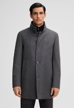 Cappotto grigio in lana con colletto alto, dotato di bottoni e tasche laterali. Texture liscia e design su misura. Stile classico e versatile.