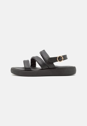 Sandale noire avec trois brides rembourrées et une boucle dorée sur une semelle épaisse, montrée de profil sur un fond uni.