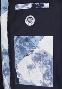 Tissu à motifs bleu et blanc avec un fond navy. Présente un logo avec du texte, une poche et un accent transparent avec des instructions d'entretien.