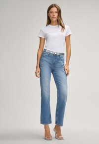 Lichtblauwe recht gesneden jeans gecombineerd met een witte T-shirt met reliëftekst, onderbroken door een zilveren studs riem en sleehakken.