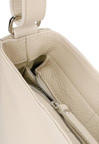 Interiér béžové texturované kožené kabelky, obsahující kapsu na zip a zelenou podšívku. Kožený popruh se stříbrnými akcenty.