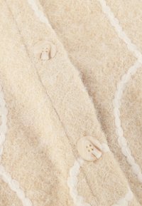 Beige gebreide cardigan met een zachte, gestructureerde wolstof, decoratieve witte piping en ronde crèmekleurige knopen met twee gaten.