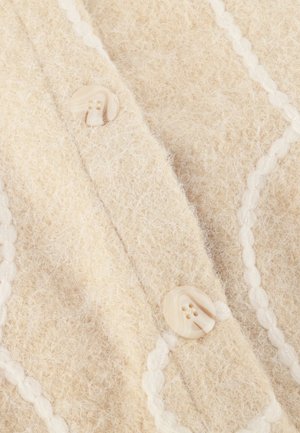 Beige knit cardigan featuring a soft, textured wool fabric, decorative white piping, and round cream-colored buttons with two holes.