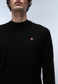 Zwarte lange mouwen trui met een ronde hals, gemaakt van gebreide stof, met een klein geborduurd vlagdetail op de borst.