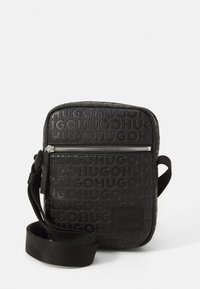 Borsa a tracolla compatta nera con motivo logo "HUGO" in rilievo, tasca frontale con zip e tracolla regolabile.