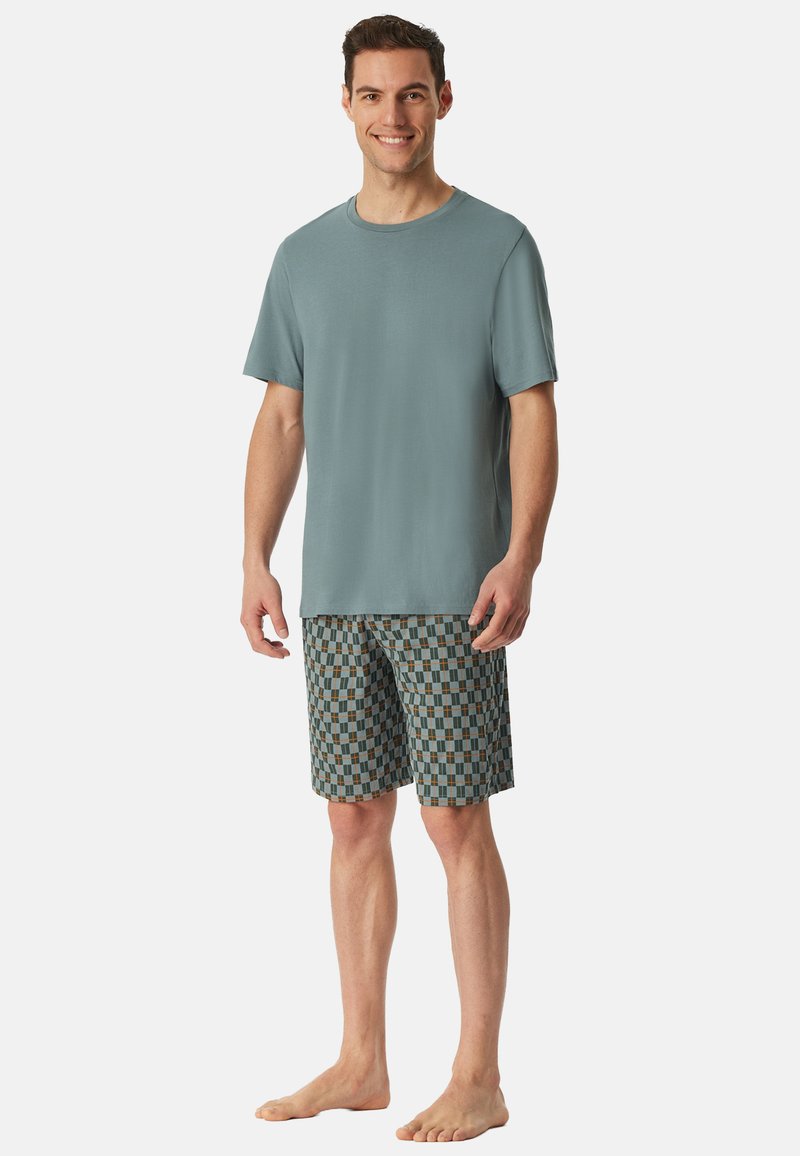 Tenue masculine composée d'un t-shirt col rond teal et de shorts à carreaux dans des tons de bleu, vert et marron, avec une coupe décontractée.