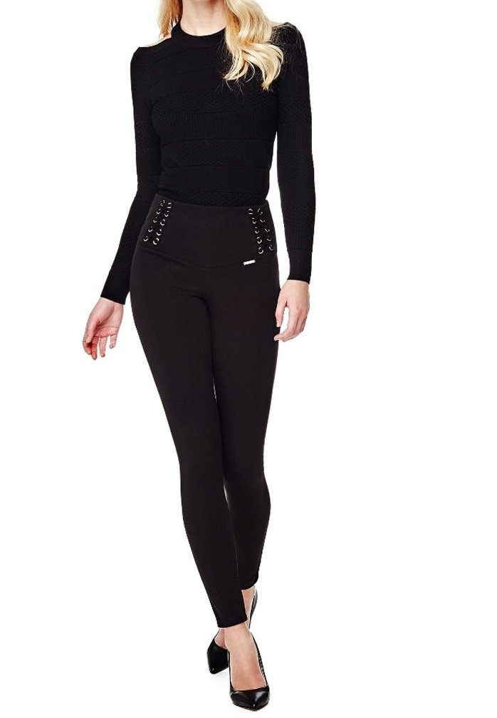 Femme portant un haut ajusté à manches longues noir et un pantalon noir taille haute avec des détails à lacets, assortis à des escarpins noirs pointus.