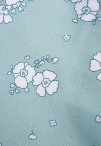 Tessuto azzurro chiaro con una superficie finemente strutturata, caratterizzato da motivi floreali bianchi e piccoli dettagli in contorni blu più scuri.