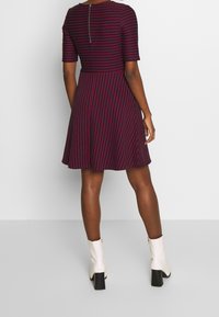 Marinblau- und rotgestreiftes Kleid mit kurzen Ärmeln, ausgestelltem Rock und einem Reißverschluss auf dem Rücken. Hergestellt aus einem weichen, strukturierten Stoff.