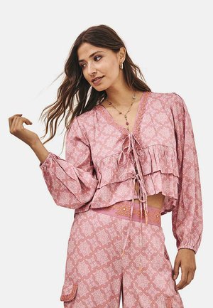 Blusa corta rosa con volantes en capas, mangas largas y escote en V. Presenta un patrón floral y un lazo en la parte delantera. Tela ligera.