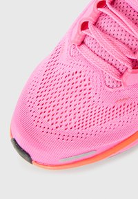 Gros plan sur une chaussure de course en maille respirante rose avec des lacets et un détail de semelle orange.
