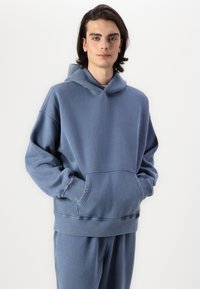 Hoodie bleu lourd avec une grande poche avant, des poignets côtelés et une capuche réglable avec cordon. Matière douce en mélangé de coton.