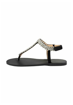 Sandale noire plate avec un design à t-strap, présente une rangée de strass clairs attachés le long de la sangle supérieure, semelle en caoutchouc.