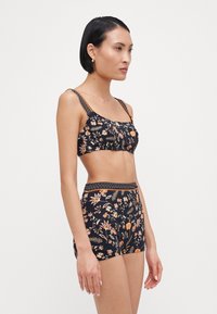 Gėlių rašto dviejų dalių maudymosi kostiumėlis su juodu pagrindu, oranžinėmis ir baltomis gėlėmis, susirankiojusia juosmens juosta ir reguliuojamomis petnešėlėmis.