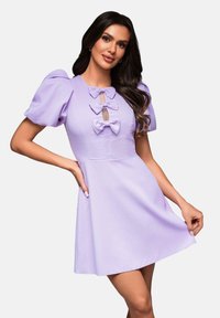 Robe courte lilas avec des manches bouffantes, comportant trois nœuds décoratifs et une découpe en forme de clé au niveau du décolleté. Texture de tissu lisse.