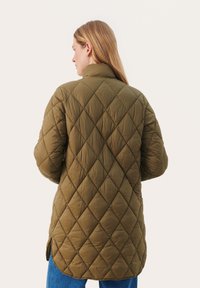 Olivgrüne gesteppte Jacke mit hohem Kragen, verlängertem Rücken, seitlichen Schlitzen und Rautenmuster. Glatte Textur mit leichtem Design.