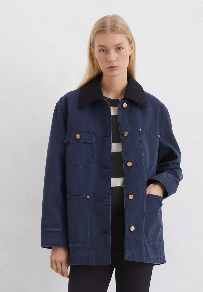 Veste bleu marine avec un col noir, fermeture à boutons à l'avant et quatre poches. Fabriquée en tissu durable, elle présente une coupe décontractée et une texture lisse.